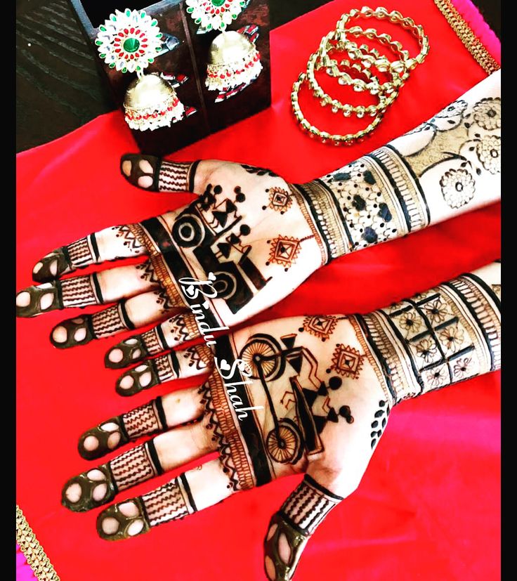 two hands with henna tattoos and jewelry on top of a red cloth covered table