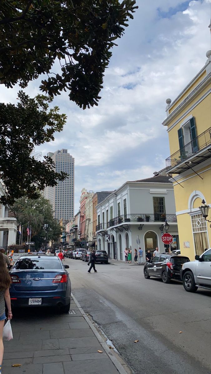 cars parked on the side of a street next to tall buildings and people walking down the sidewalk