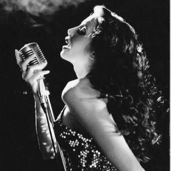 a woman holding a microphone in her right hand and singing into the microphone with both hands