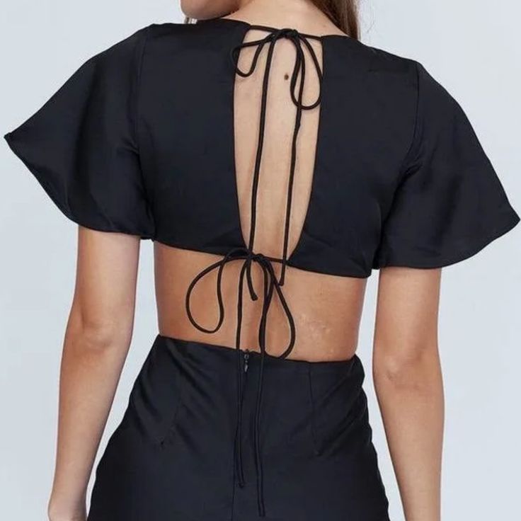 the back of a woman's black dress with an open neck and tie at the waist