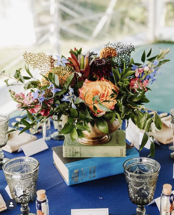 a blue table topped with books and vases filled with different types of flowers on top of each other