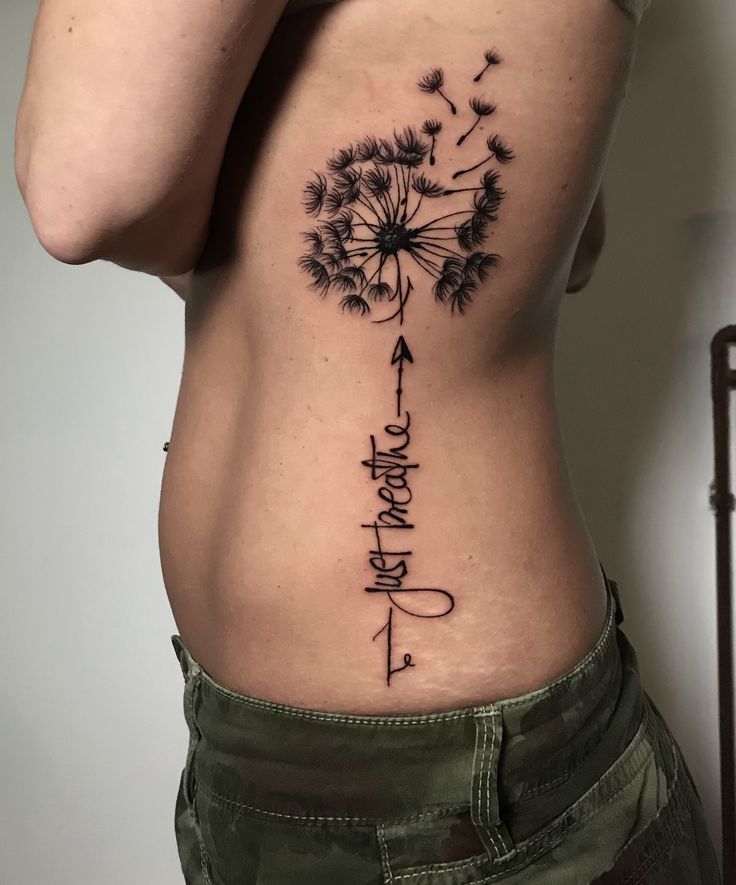 a woman's back with a dandelion tattoo on her lower body and words written in cursive writing