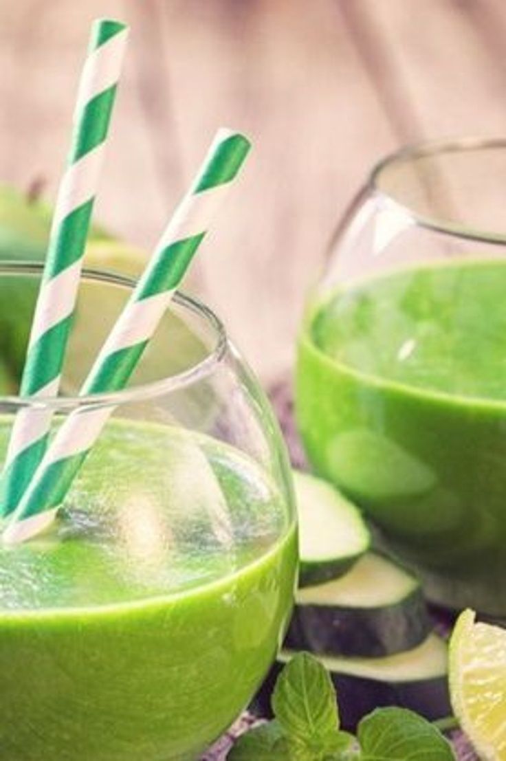 two glasses filled with green smoothie next to sliced limes and cucumbers