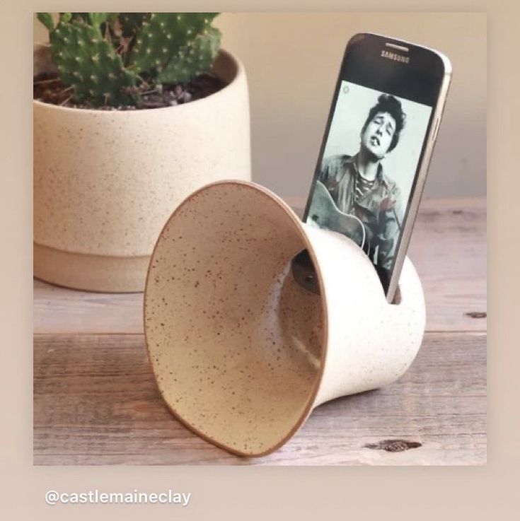 a cell phone sitting in a cup next to a cactus