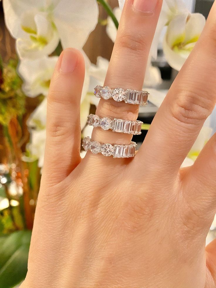 a woman's hand with three rings on it and flowers in the back ground