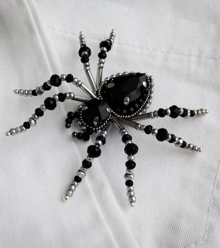 a black spider brooch sitting on top of a white shirt covered in beads and crystals