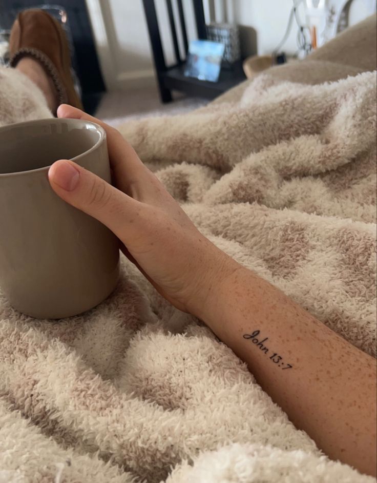 a woman's hand holding a coffee cup on top of a bed