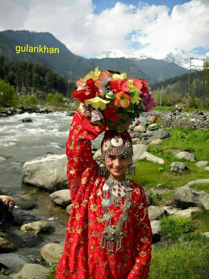 a woman in red dress standing next to a river with flowers on it's head