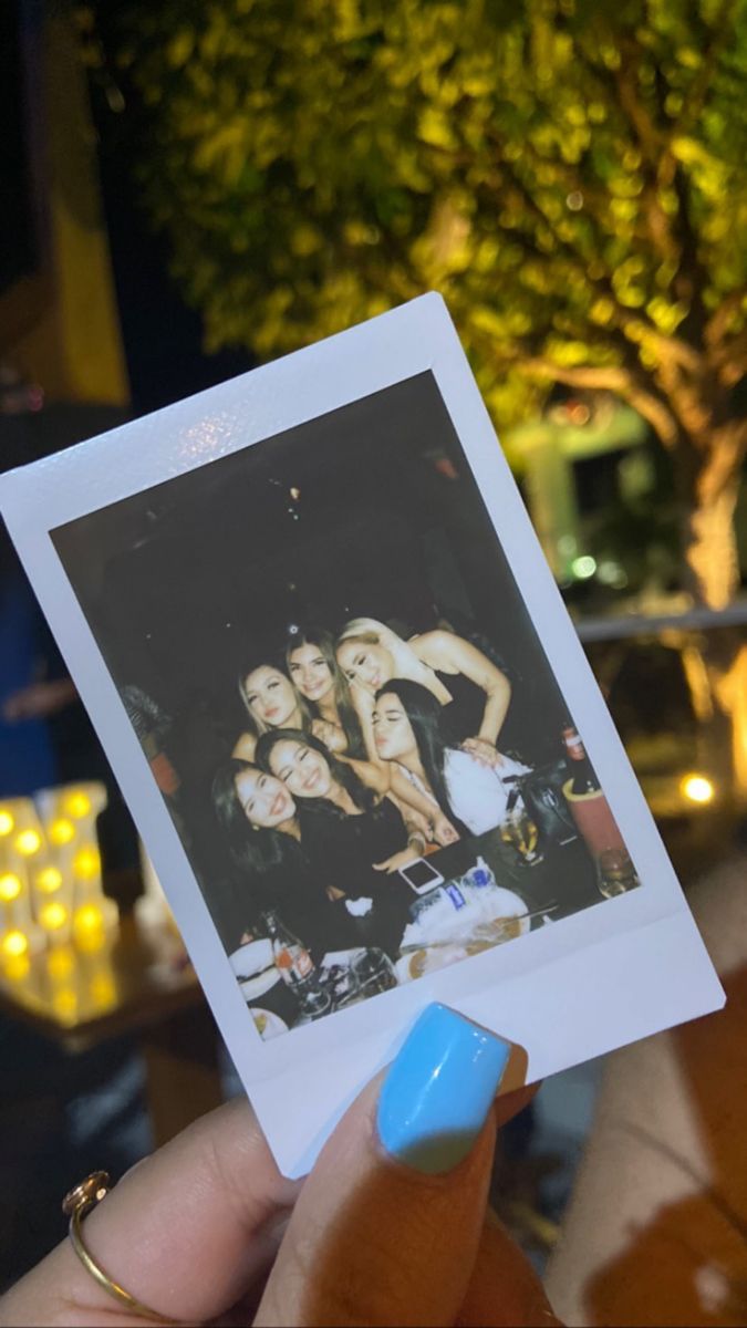 a person holding up a polaroid photo in front of some trees at night time