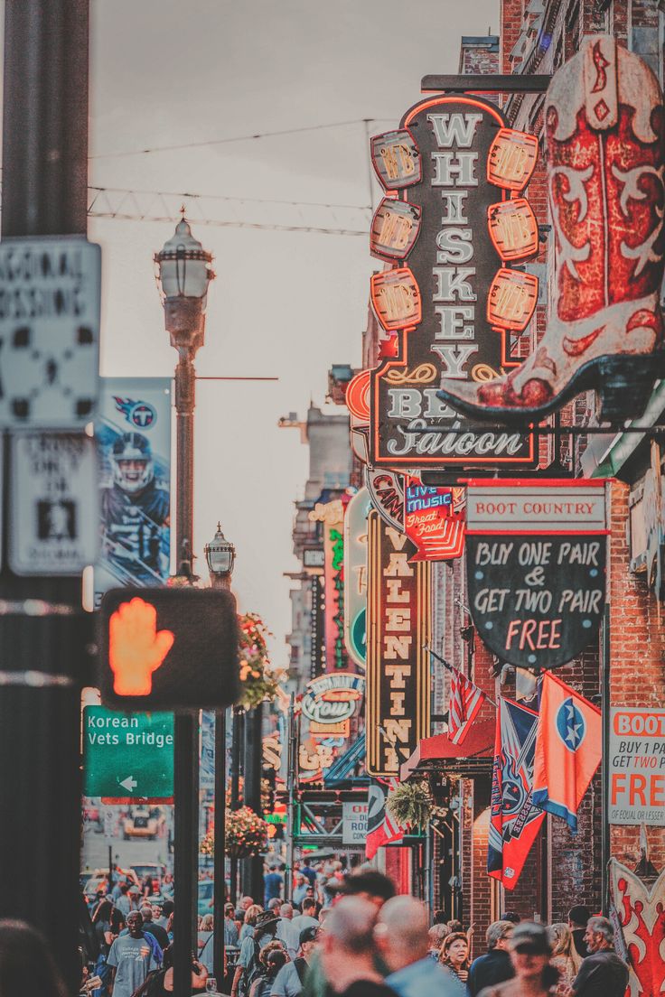 a crowded city street filled with lots of signs and people walking down the side walk