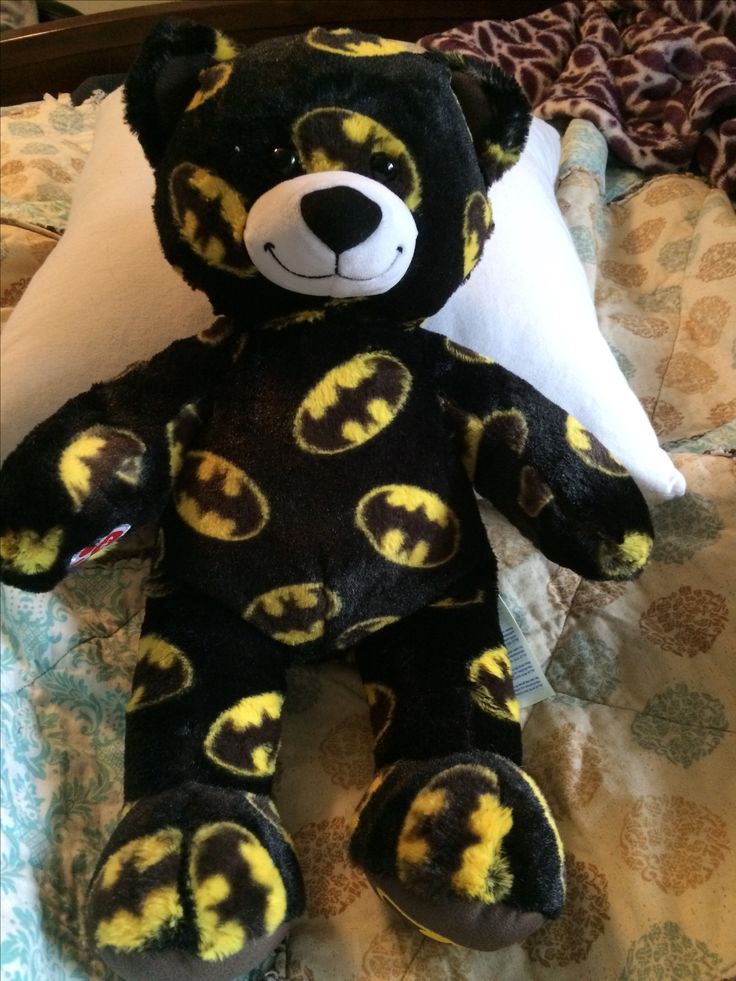 a black and yellow teddy bear sitting on top of a bed next to a pillow