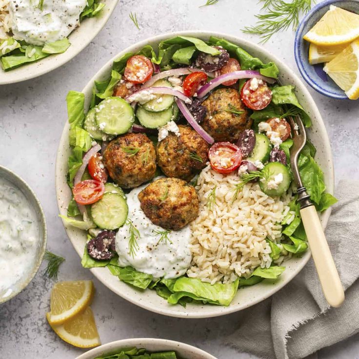 two bowls filled with salad and meatballs next to lemon wedges on the side