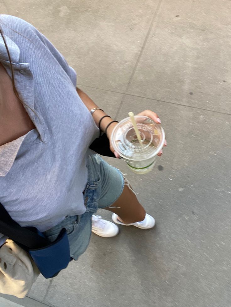 a woman sitting on the ground drinking from a water bottle and holding a cup in her hand