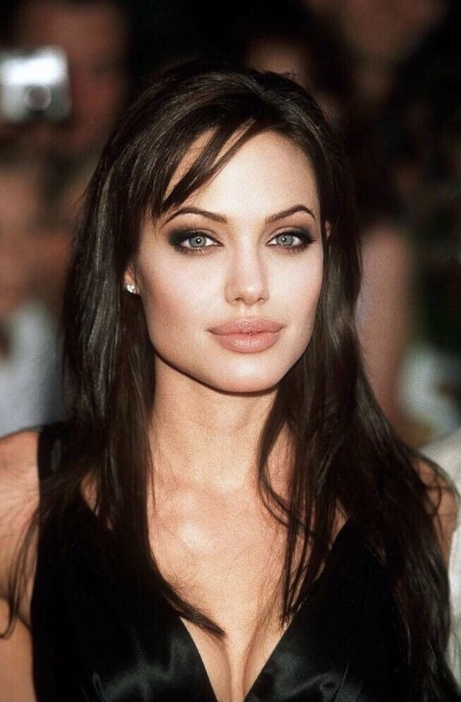 a close up of a person wearing a black dress and posing for a photo with people in the background