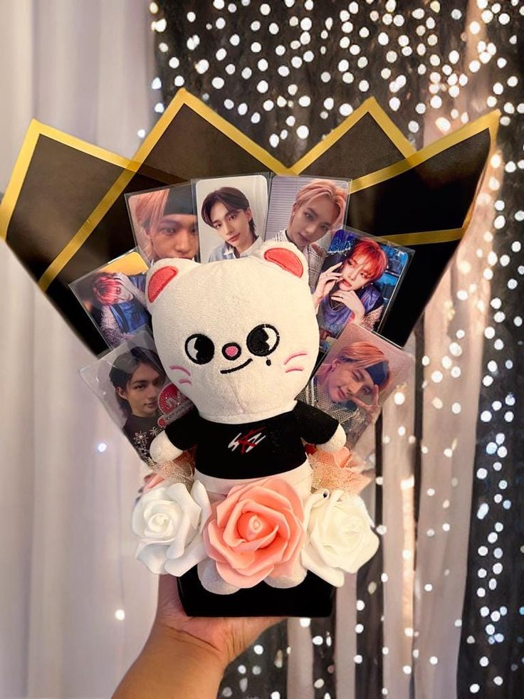 a person holding up a stuffed animal with pictures on it's face and flowers in front of them