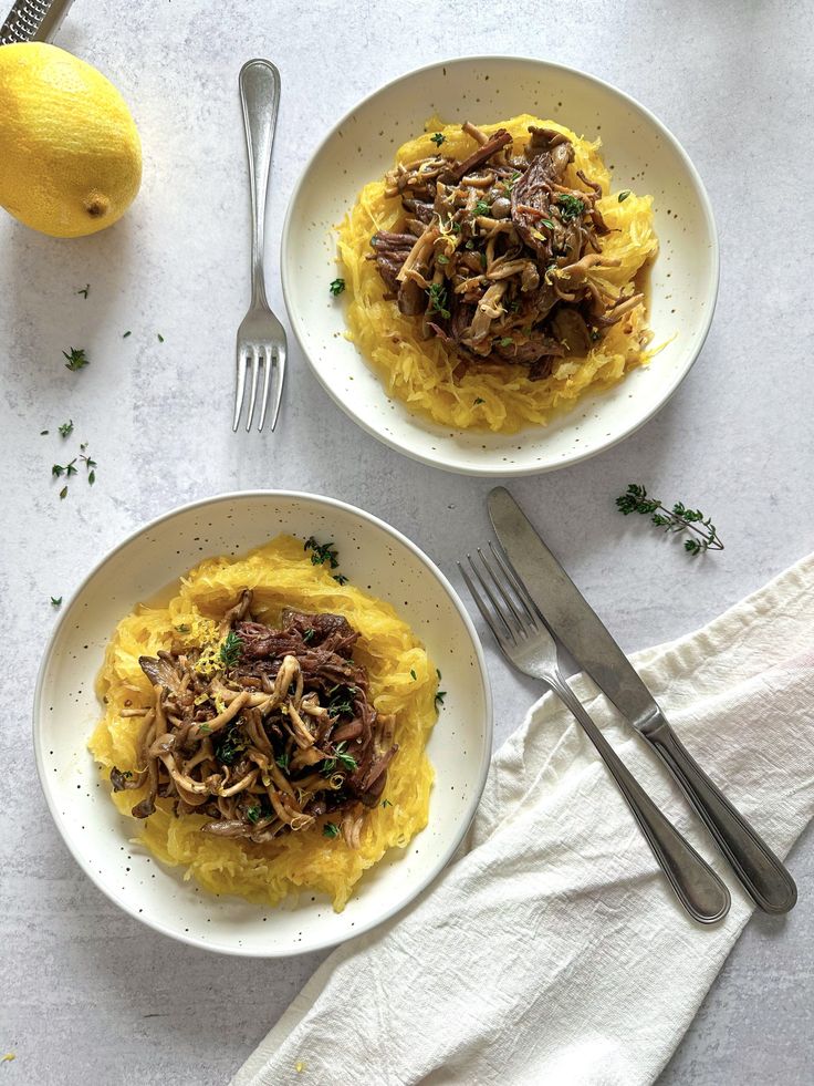 two white plates topped with spaghetti and meat on top of a table next to lemons