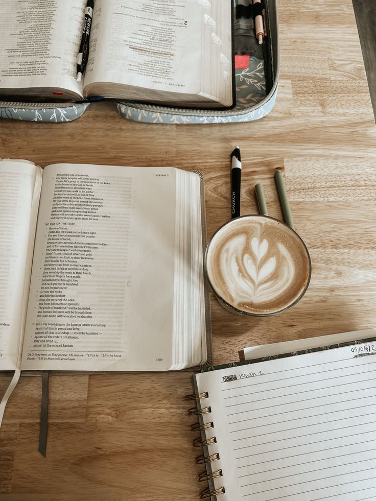 an open book and cup of coffee sit on a table next to two notebooks