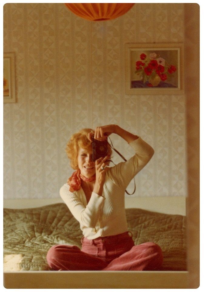 a woman sitting on top of a bed while holding a camera up to her face