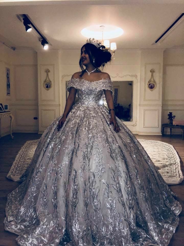 a woman in a silver ball gown standing on a wooden floor with her hands behind her back