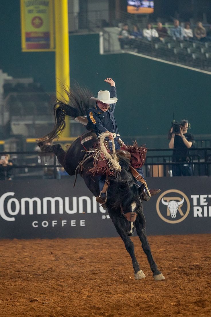 a man riding on the back of a black horse in an arena at a rodeo