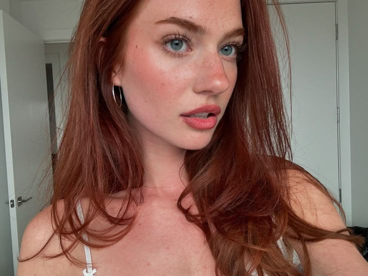 a woman with red hair and blue eyes is looking at the camera while wearing earrings