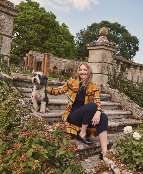 a woman sitting on steps with her dog in front of an old stone building and garden