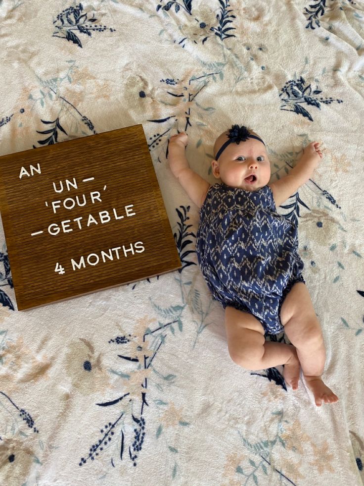 a baby laying on top of a bed next to a sign that says an uni four - getable 4 months