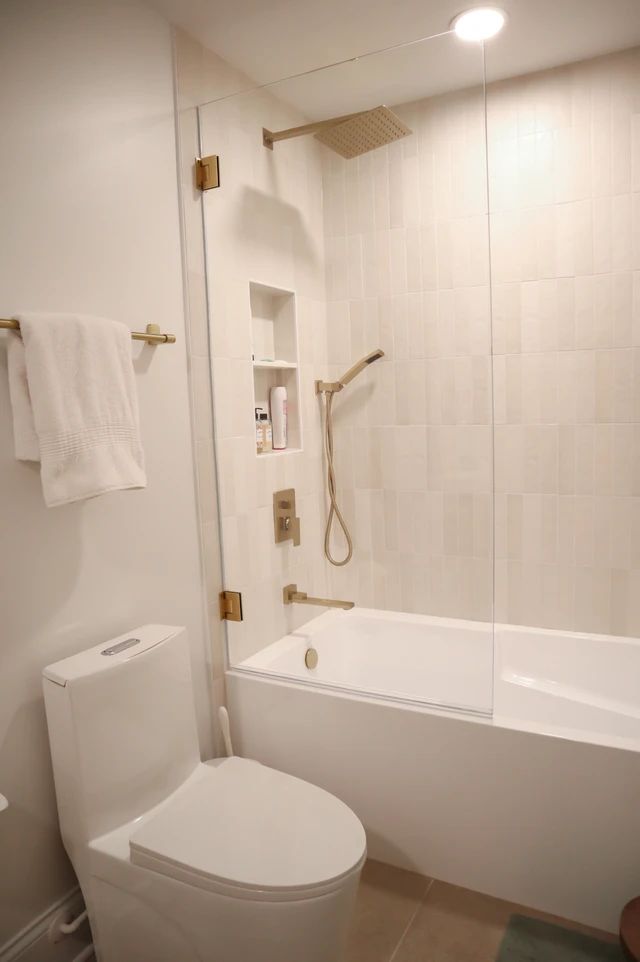 a white toilet sitting next to a bath tub in a bathroom under a light fixture