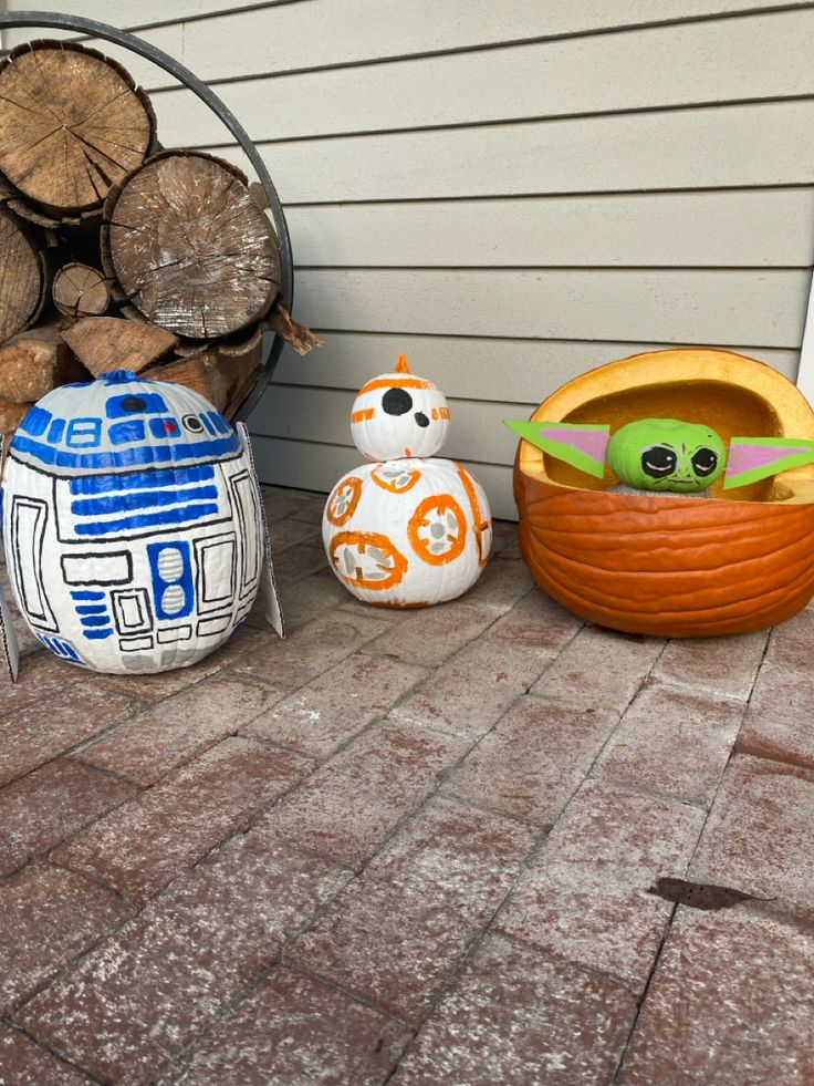 star wars themed pumpkins sit on the ground next to firewood stacked in front of a house