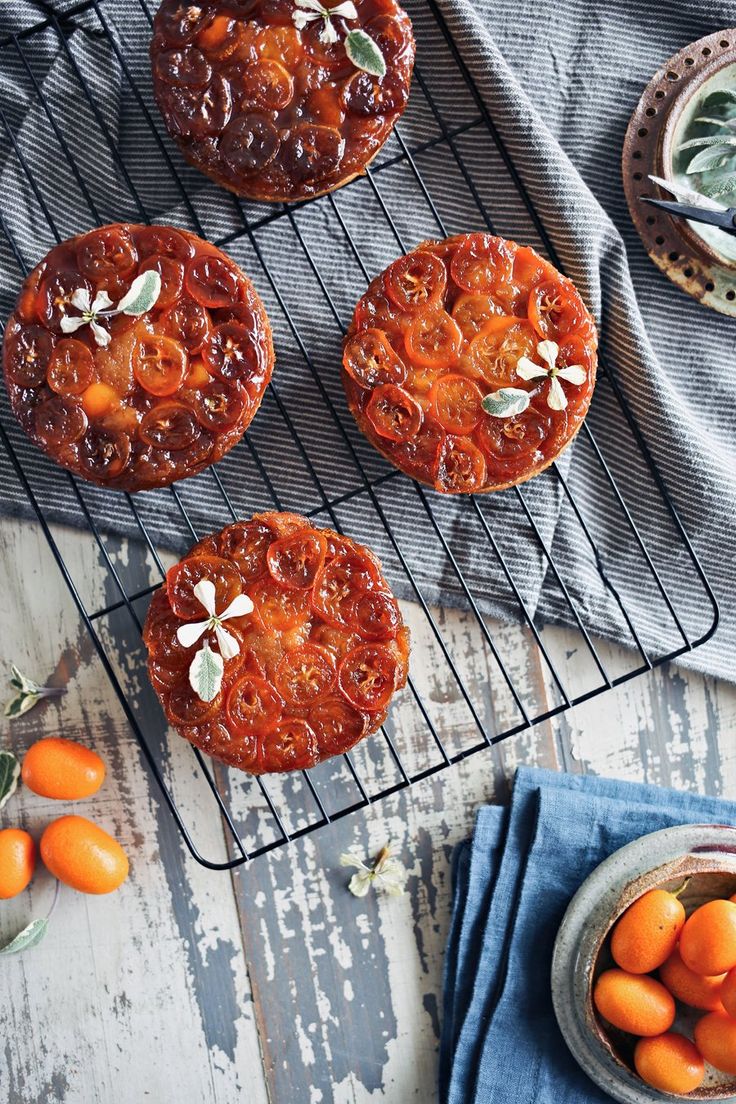 three orange cakes sitting on top of a cooling rack next to small bowls of fruit