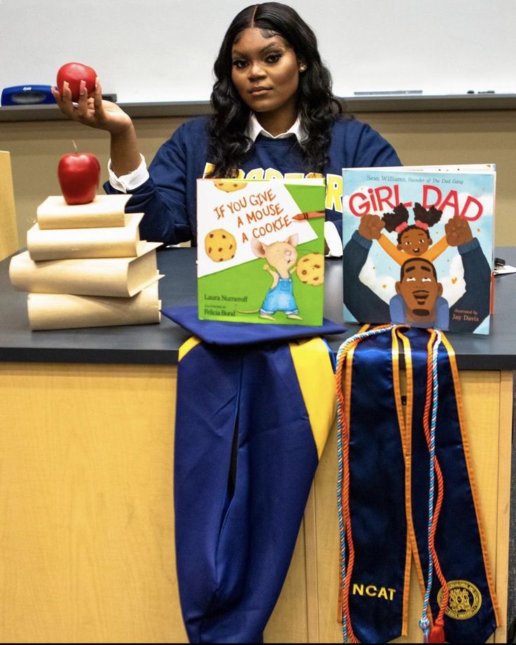 a woman sitting at a desk holding up two children's books and an apple