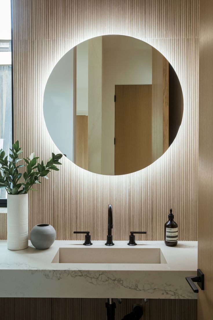 a bathroom sink with a round mirror above it and a vase on the counter next to it