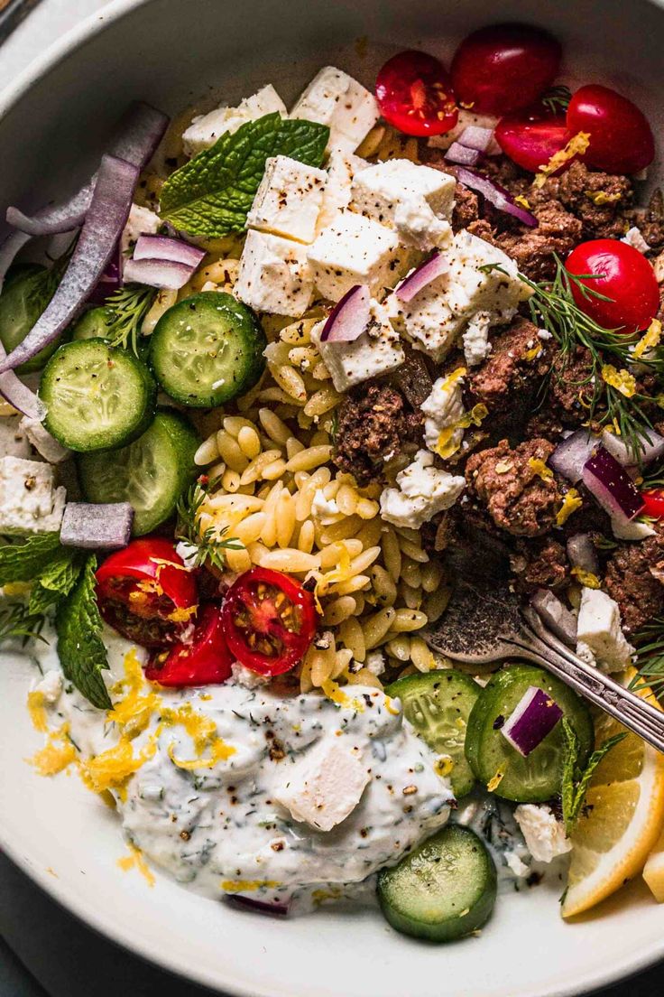 a white bowl filled with pasta, meat and veggies on top of a table