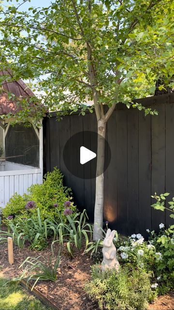 a backyard garden with trees and flowers in the foreground, next to a wooden fence