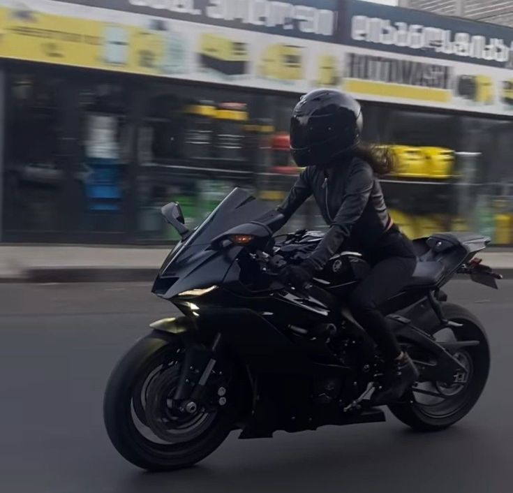 a person riding on the back of a black motorcycle down a street in front of a store