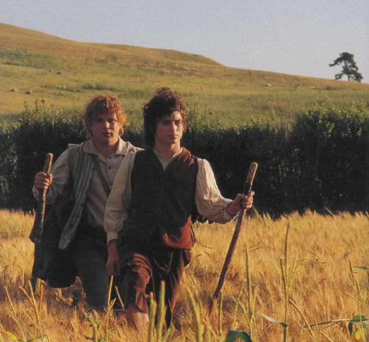 two young men walking through a field holding stick