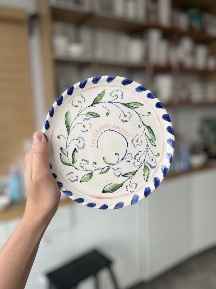 a hand holding up a decorative plate in front of a shelf with shelves and chairs