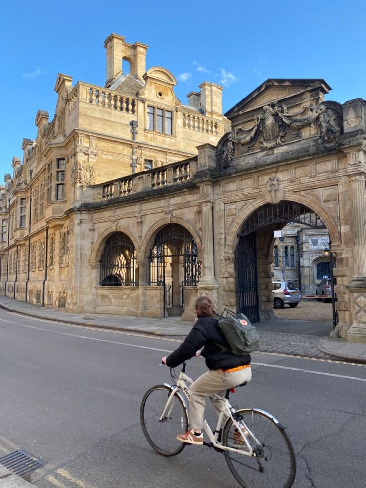 a man riding a bike down a street in front of a large building with arches