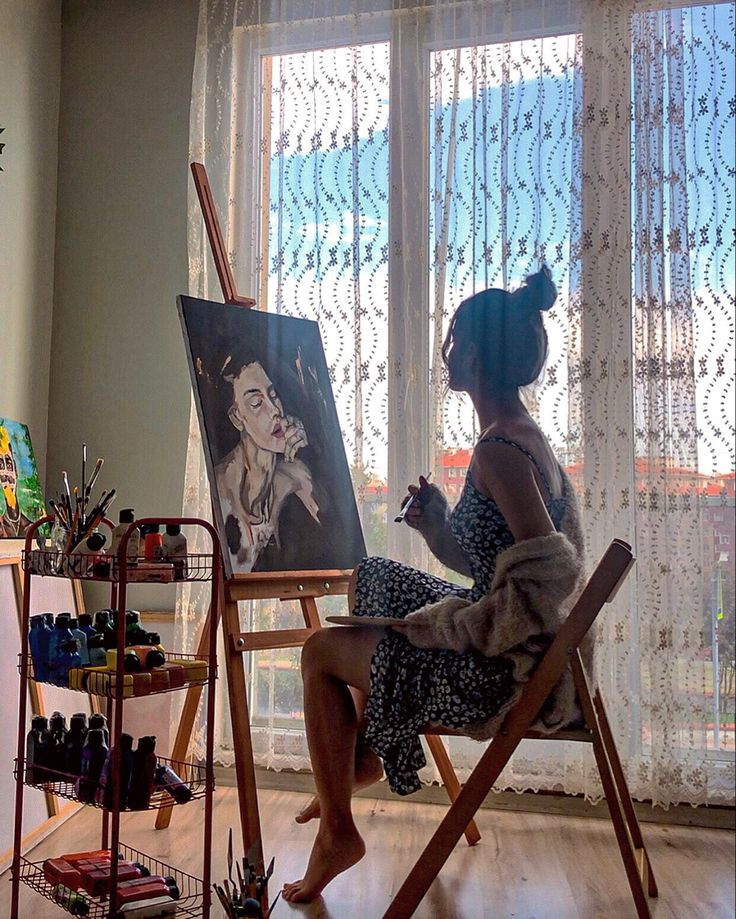 a woman is sitting in a chair with an easel and painting on the wall