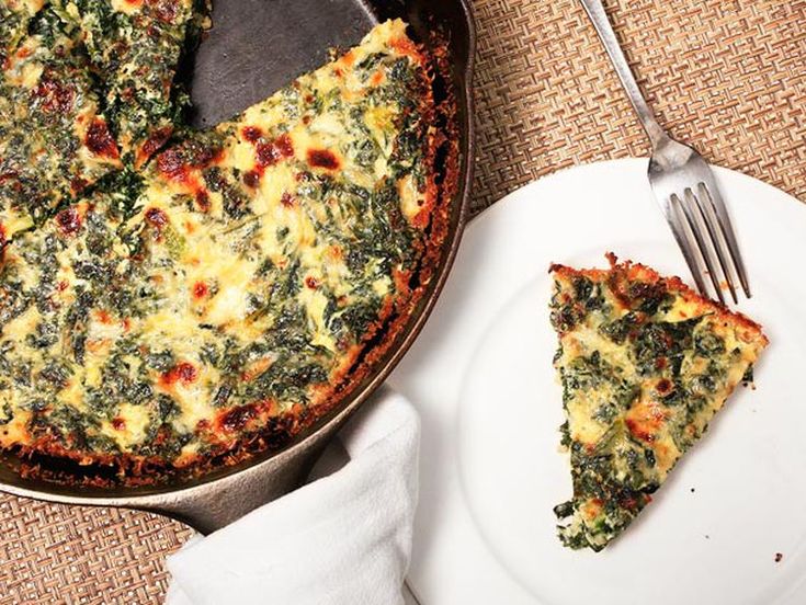 a pizza with cheese and spinach is on a plate next to a fork and knife