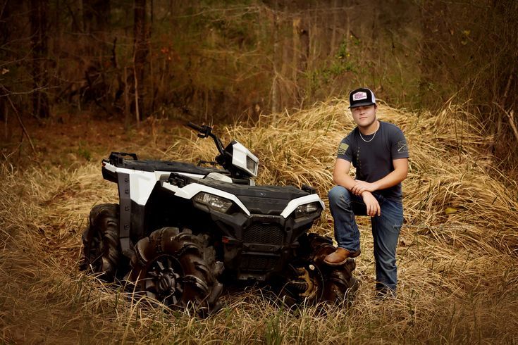 a man sitting next to an atv in the grass