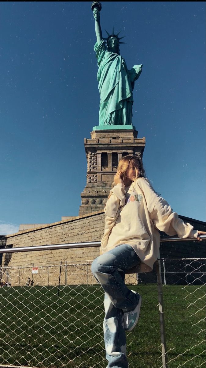 a woman leaning on a fence in front of the statue of liberty, new york city