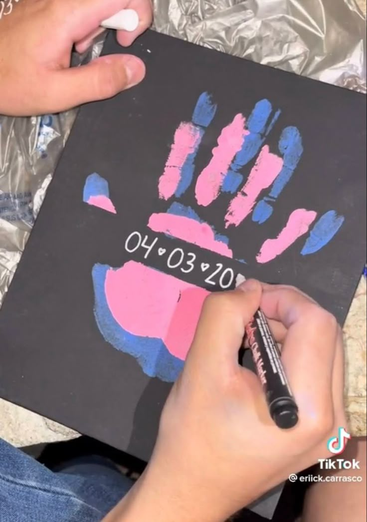 someone is drawing on a piece of black paper with pink and blue handprints