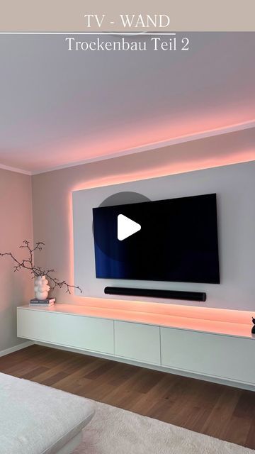 there is a tv on the wall in this living room with pink walls and white furniture