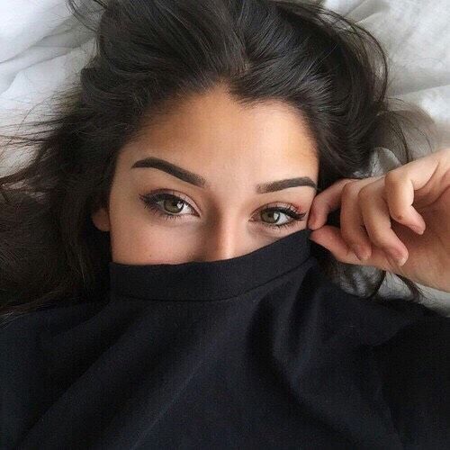 a woman laying on top of a bed with her eyes open and covering her face