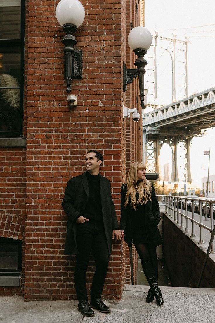 a man and woman standing next to each other in front of a tall brick building