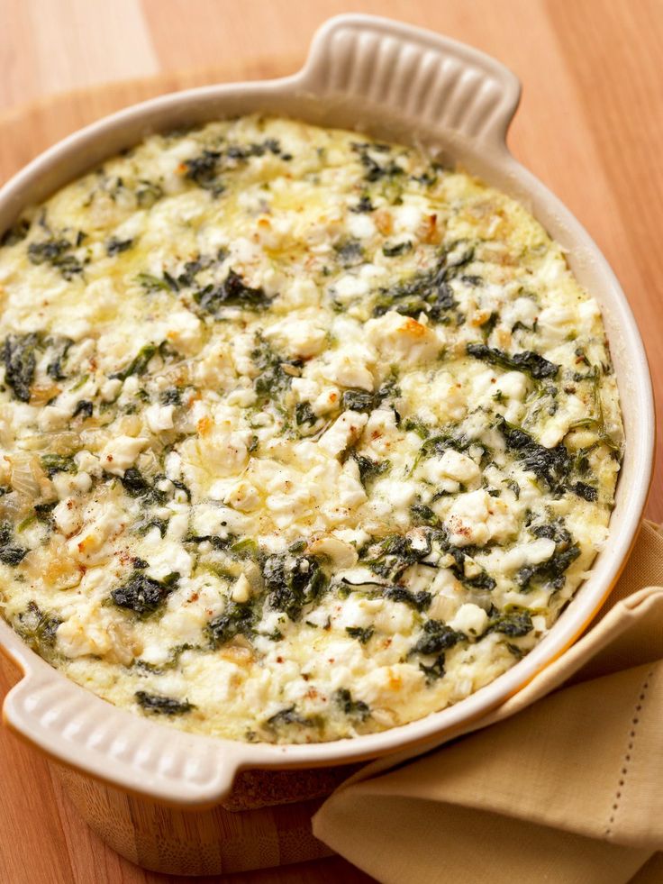 a casserole dish with spinach and cheese in it on a wooden table