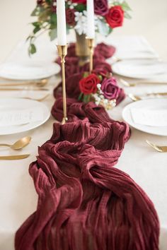 the table is set with white plates and red napkins, gold place settings and candles