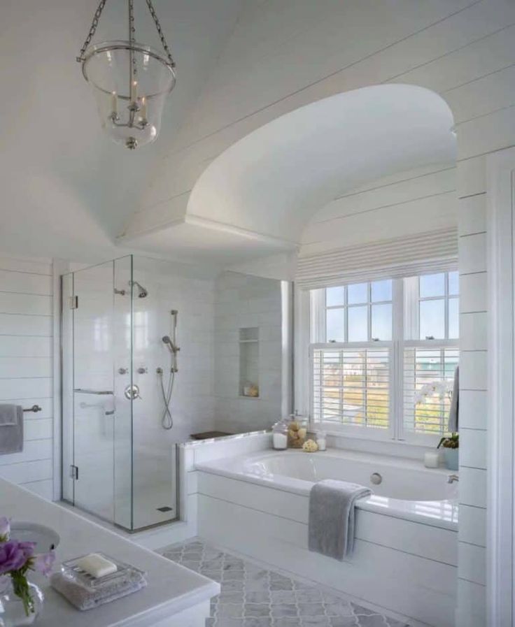 a large white bathroom with an arched window and chandelier hanging from the ceiling