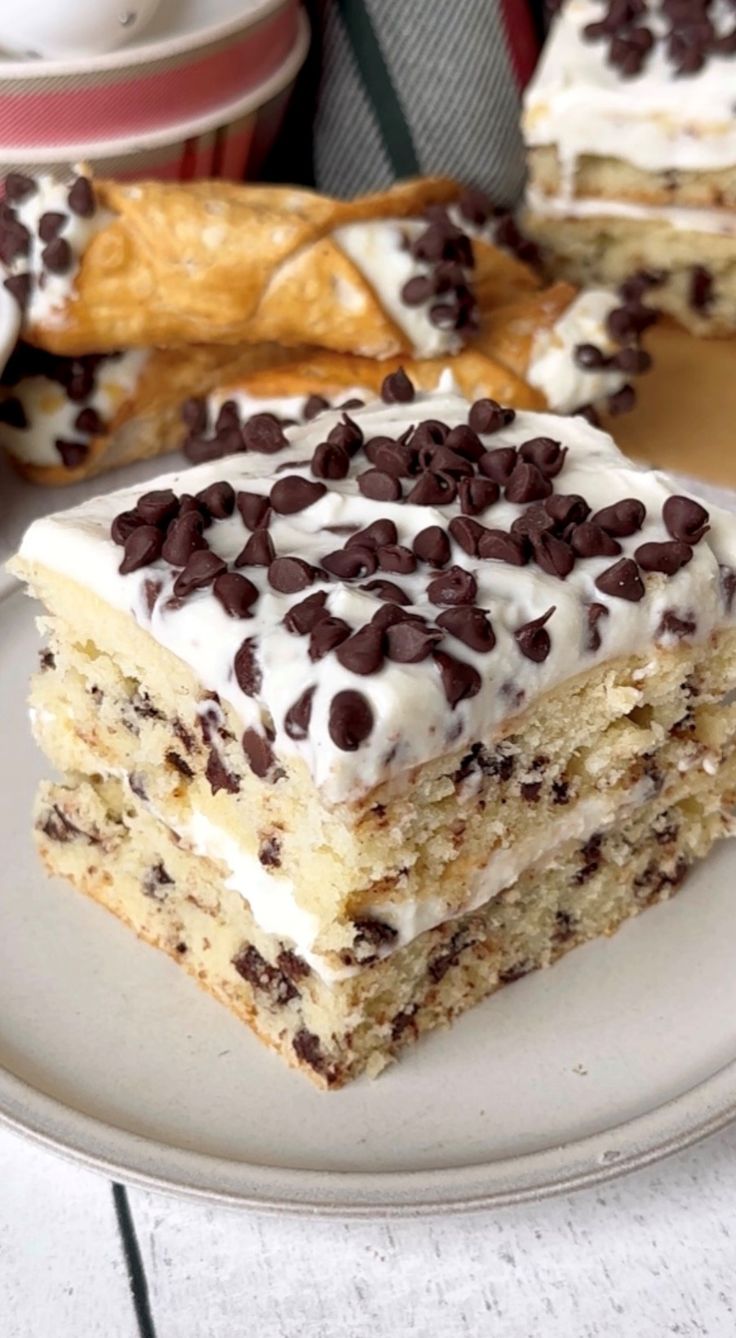 a piece of cake on a plate with chocolate chips and frosting, sitting on a table